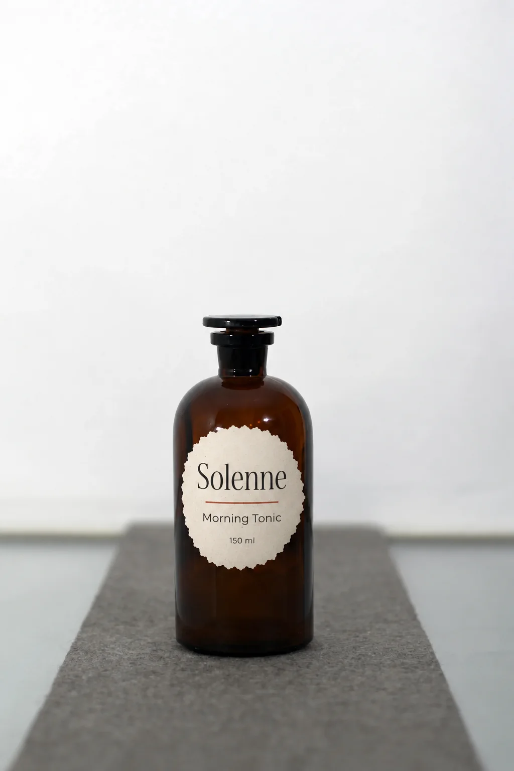An amber apothecary bottle of Morning Tonic with a round label, on a grey runner