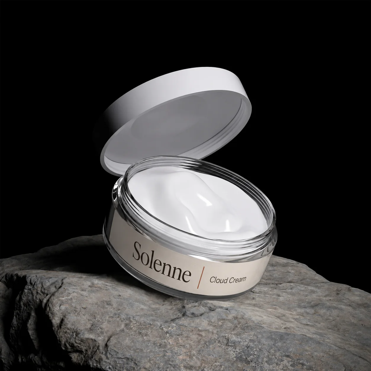 The open jar of Cloud Cream, its lid tipped back, on a rock in low light